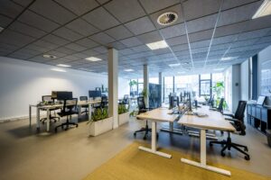 Moderne, open kantoorruimte aan de De Ruijterkade met werkplekken, bureaustoelen en groene planten.